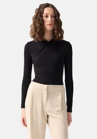 Czarny bodysuit z długim rękawem o kroju kopertowym, zestawiony z jasnymi spodniami w paski, które mają wysoki stan i zaszewki.