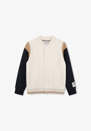 Beige varsity-stil jakke med marineblå ærmer og tan skulderlapper, frontknapper med trykknapper og to forlommer.
