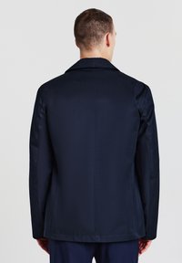 Giacca blu navy con una texture liscia e opaca, dotata di colletto a rotondo, taglio dritto e senza hardware o motivi visibili.