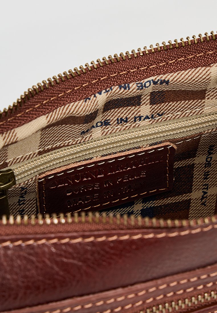 Wnętrze brązowej skórzanej torby z zamykaną kieszenią, w kratkowanej podszewce i wytłoczonym oznaczeniem "Skóra naturalna, wyprodukowano we Włoszech."