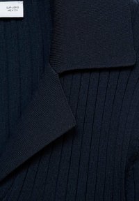 Tissu tricoté côtelé bleu marine foncé avec un large col et une petite étiquette blanche indiquant la taille EUR USA S MEX CH.
