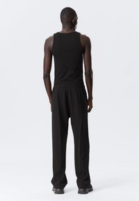 Zwarte tanktop en loszittende zwarte broek van zachte stof, met een elastische tailleband en eenvoudige snit, gezien van achteren.