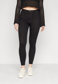 Černé skinny džíny vyrobené z elastického materiálu, s předními kapsami, zipem a knoflíkovým zapínáním. V kombinaci s bílými platformovými teniskami.