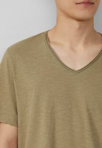 Olijfgroen v-hals t-shirt van zacht, gestructureerd materiaal met korte mouwen en een comfortabele pasvorm, voorzien van nette stiksels langs de halslijn.