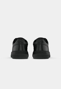 Zapatillas de cuero negro con una textura suave, que cuentan con una suela de goma resistente, detalles del logo en la parte trasera y un diseño minimalista.