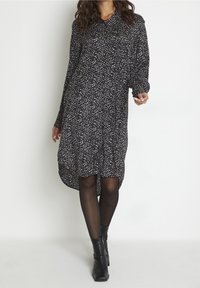 Robe noire à motifs avec des taches blanches et roses, manches longues, col boutonné, ourlet arrondi, et assortie à des bottines noires.