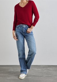 Röd V-ringad tröja kombinerad med löst sittande ljusblå jeans. Outfiten har en avslappnad design med mjuka texturer och minimala detaljer.