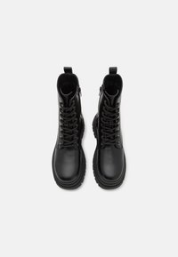 Bottines en cuir noir avec un bout rond, un laçage sur le devant, des zips sur le côté et des semelles en caoutchouc épaisses et texturées. Fini lisse, détails minimalistes.
