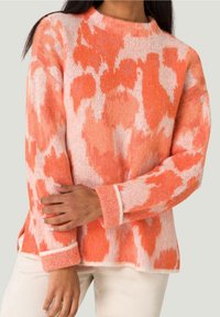 Ett mönstrat svetttröja i orange och rosa, med en mjuk, texturerad tyg, vida ärmar och en rund halsringning med kontrasterande kant.