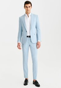 Jasnoniebieski garnitur o dopasowanym kroju, zapinany na jeden guzik, z pasującymi spodniami. Biała koszula pod spodem, czarny pasek i czarne buty.