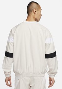 Giacca sportiva bianca con strisce nere e bianche sulle maniche, polsini e vita elasticizzati. Texture liscia, design leggero e vestibilità rilassata.