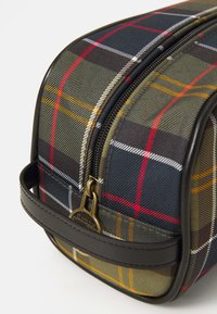 Tartán mintás mosdószer táska bőrfogantyúval és réz cipzárral, amelyen a "Barbour" felirat található, fehér háttéren.