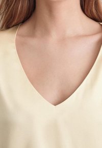 Blouse à col en V de couleur jaune clair, fabriquée dans un tissu doux et lisse. L'encolure présente un design épuré et discret. Pas de motifs ni d'accents.
