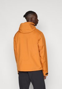 Oranje waterdichte jas met een capuchon, voorzien van een gestructureerde stof, een verlengde achterkant en zwarte polsaccenten.