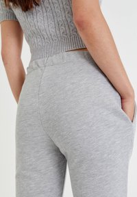 Helle graue Jogginghosen aus einem weichen Baumwollmischgewebe, mit einem elastischen Bund und seitlichen Taschen, die eine glatte Textur und eine lockere Passform bieten.