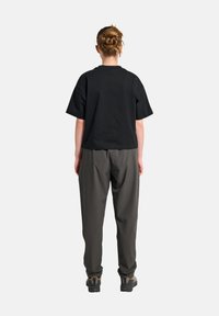 Zwarte katoenen t-shirt met korte mouwen, gecombineerd met losse grijze broeken. Het model draagt zwart-grijze schoenen. Eenvoudig ontwerp, geen patronen.