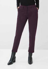 Violette, texturierte Hose mit schmalem Schnitt, ausgestattet mit einem Knopfverschluss und Seitentaschen, kombiniert mit schwarzen, hohen Stiefeletten.