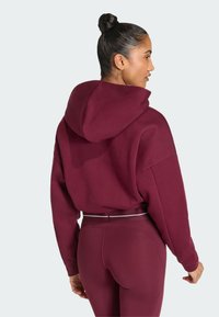 Bordowa bluza z kapturem o luźnym kroju i dużym kapturze, z prążkowanymi mankietami. W połączeniu z dopasowanymi legginsami i cienkim białym paskiem w talii.