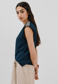 Navyblaues Kurzarmoberteil mit lockerer Passform, das bestickte Akzente auf der Schulter hat. Glattes Material, schlichtes Design, eleganter Abschluss.