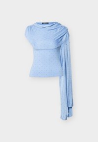 Ανοιχτό γαλάζιο τοπ με ένα μανίκι, μικρές μαύρες πουά και ριγωτό υφάσμα που συγκεντρώνεται από τον ώμο μέχρι τον καρπό.