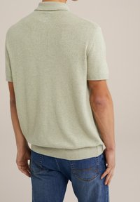 Ljusgrön pikétröja med korta ärmar och texturerad stickad design, med ribbad krage och nederkant. Bärs med blå jeans.