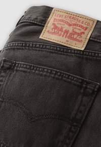 Mustad teksapüksid tikk-tagumiste taskutega ja pruun Levi Strauss & Co. silt, millel on kujutatud kahte hobust pükse lahutamas.