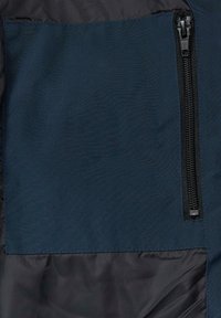 Granatowy materiał o gładkiej fakturze z kieszenią na suwak po prawej stronie, kontrastujący z matowym tłem.