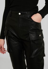 Černé kožené cargo kalhoty s hladkým povrchem, vybavené bočními kapsami a předním zapínáním na patentku. Zúžený design zvýrazňuje postavu.