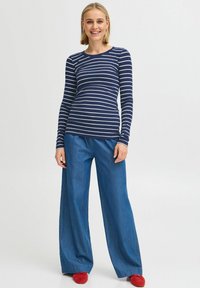 Skarpetka w niebiesko-białe paski z długim rękawem, zestawiona z jasnoniebieskimi spodniami dżinsowymi typu wide-leg i jaskrawoczerwonymi butami. Prosty wzór, casualowy styl.