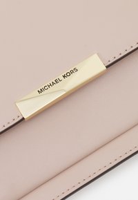 Clutch in pelle rosa chiaro con una placca in metallo dorato con la scritta "MICHAEL KORS" incisa. Texture liscia e cuciture ordinate lungo i bordi.