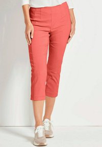 Koraal kleurige capri-broek van lichtgewicht stof, met een gladde textuur, met een platte voorkant en omgezoomde manchetten, gecombineerd met beige sneakers.