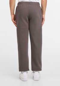 Person står i grå lige sweatpants, hvide sokker og hvide sneakers foran en ensartet lys baggrund.