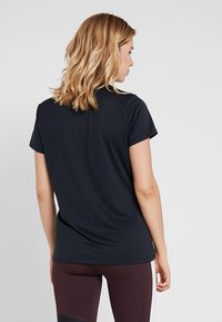 Schwarzes Kurzarm-T-Shirt mit glatter Textur und rundem Halsausschnitt, von hinten betrachtet, kombiniert mit bordeauxfarbenen Leggings.