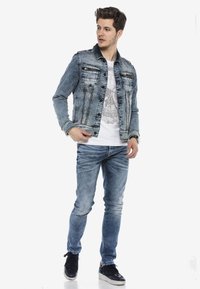 Lichtblauwe denim jack met twee borstzakken, zwarte accenten en zilveren studs. Draag boven een grafisch wit T-shirt en gecombineerd met een blauwe jeans.