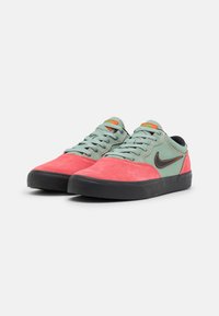 Nike sneakers with a green suede upper, pink accents, black rubber sole, and orange detailing on the tongue. Low-top design.