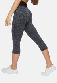 Schwarz-graue, melierte Capri-Leggings mit hohem Bund, aus dehnbarem Material gefertigt. Kombiniert mit weißen Sneakers für einen sportlichen Look.