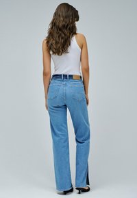 Jeans de mezclilla de color azul claro con un corte relajado y aberturas en los dobladillos, que cuentan con bolsillos traseros y una etiqueta en la cinturilla de color contrastante.