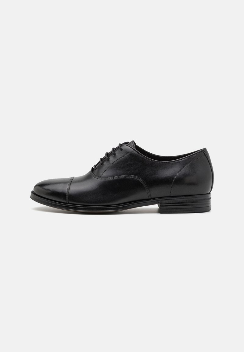 Zapato oxford de cuero negro con un acabado suave, punta redonda, cierre con cordones y tacón bajo; presenta acentos de costura en contraste.