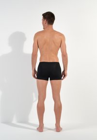 Schwarze Baumwoll-Boxershorts mit glatter Textur, mit einem schmalen Bündchen, von hinten auf einem schlichten weißen Hintergrund gesehen.