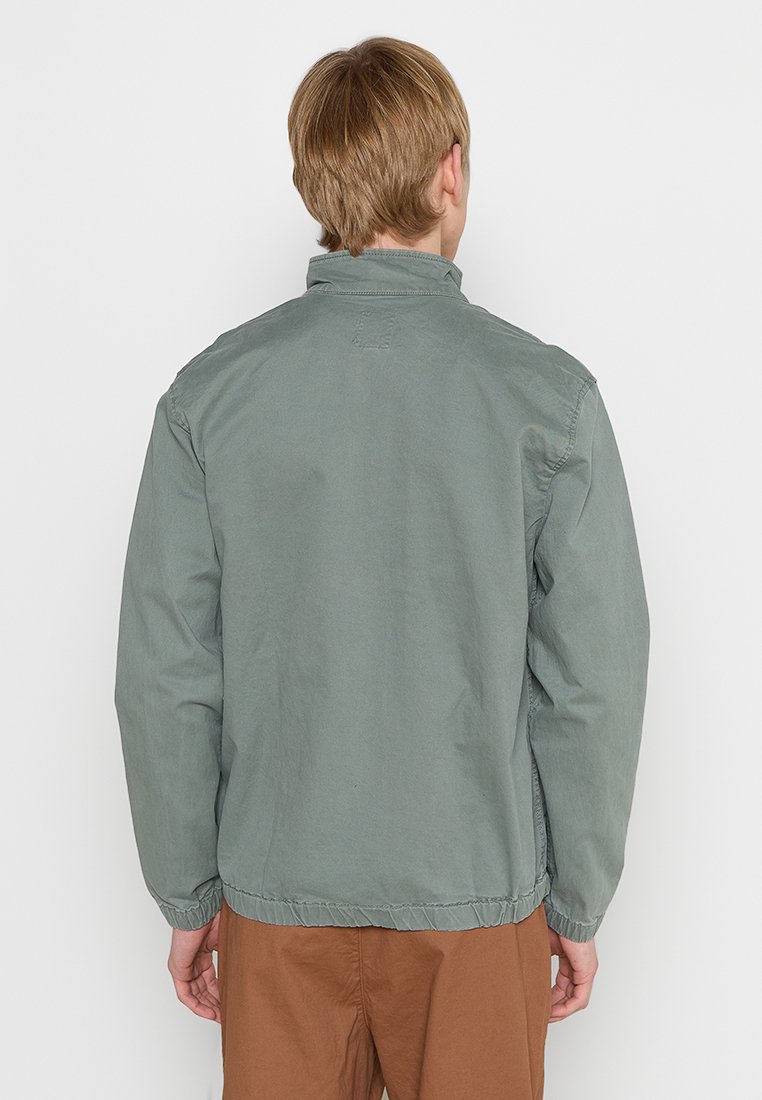 Hellgrüne, weiche Stoffjacke mit lässigem Schnitt, hochgeschlossenem Kragen und elastischen Bündchen. Mit gesticktem Detail am Hals.