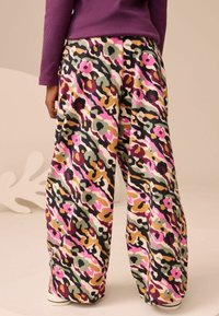 Farbenfrohe, gemusterte weite Hosen mit abstrakten Blumenschformen in Pink, Grün, Schwarz und Beige auf einem cremefarbenen Hintergrund. Weicher Stoff.