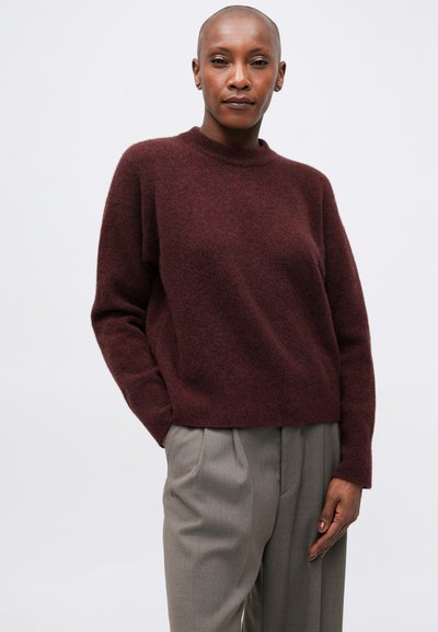 Pulover tricotat de culoare burgundă, cu gât rotund și croială lejeră, asociat cu pantaloni plisati de culoare gri deschis. Textură moale și design minimal.