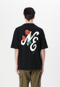 Black short-sleeve t-shirt featuring a large white graphic with the text "NO" intertwined with red roses and green leaves on the back.