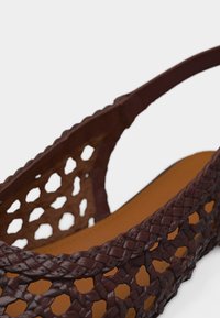 Brun vævet lædersandal med en fletrem og åbent gitterdesign, der viser den indvendige lysebrune fodseng.