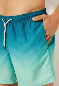 Herrbadbyxor med en gradientdesign som övergår från teal till ljusgrön. Tillverkade av ett mjukt, lätt tyg med elastisk midja.