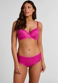 Rosa Spitzen-BH und passender Slip mit Blumenmuster, gezackten Kanten und zarten Schleifenakzenten in der Mitte vorne.