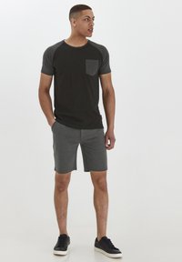 Gray T-shirt with dark gray sleeves and pocket, paired with dark gray shorts, presented with black sneakers against a neutral background.