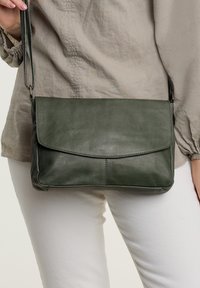 Grön läderaxelväska med vikbar flapdesgin och axelrem, med slät textur och diskreta söm-detaljer.