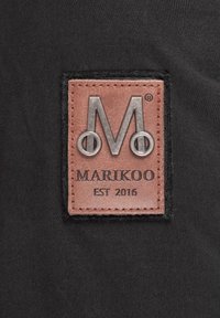 Zwarte stof met een rechthoekige bruine leren patch met een reliëf zilveren letter "M" en de tekst "MARIKOO EST 2016."