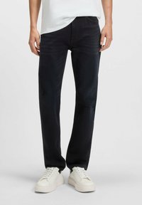 Jeans in denim scuro con vestibilità dritta, caratterizzati da una leggera scoloritura, tasche tradizionali e una finitura liscia e testurizzata. Abbinati a sneakers bianche.